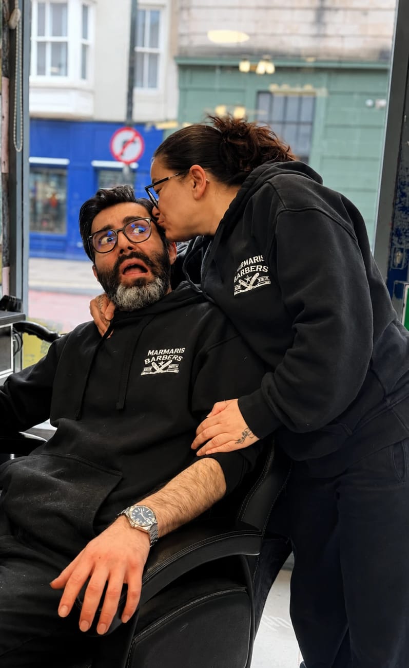 The two owners of Marmaris in the shop window, both in branded hoodies — one kissing the other on the cheek