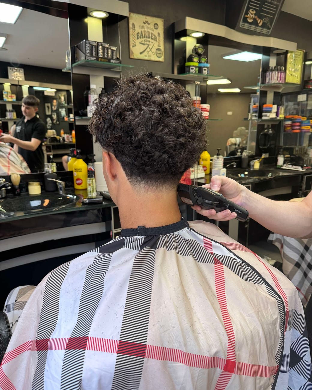 A curly cut being finished at the neckline with clippers